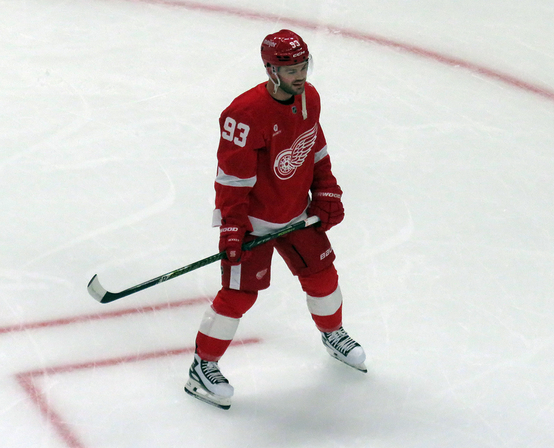 Alex DeBrincat of the Detroit Red Wings stands in a faceoff circle during pre-game warmups before a game against the Carolina Hurricanes, wearing a customized Sergei Fedorov jersey and white skates in honor of Fedorov's jersey retirement.