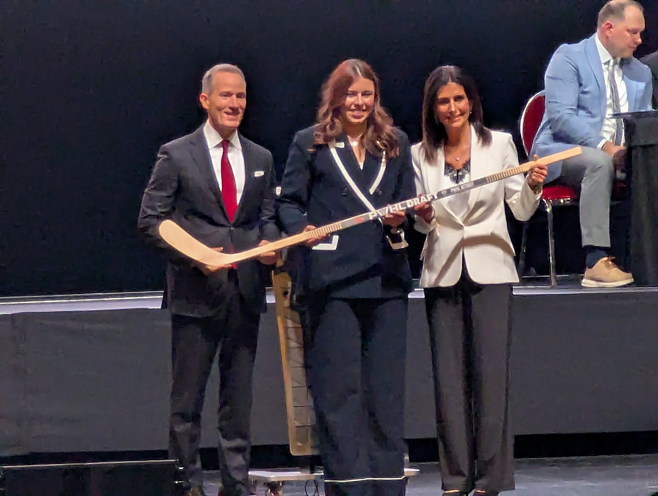 Andrea Brandli is selected fifteenth overall at the 2026 PWHL Entry Draft, flanked by Ilitch Holdings president Chris Ilitch and PWHL Detroit general manager Manon Rheaume.
