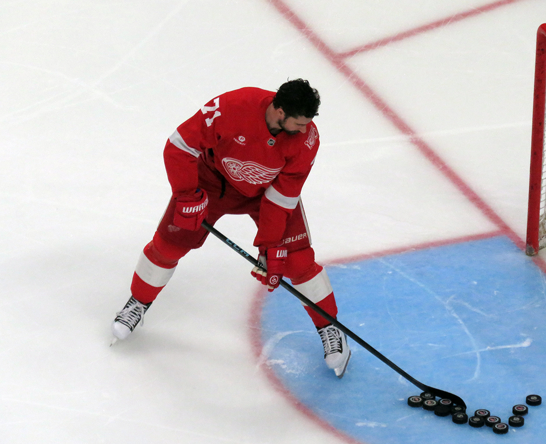 Dylan Larkin of the Detroit Red Wings clears pucks from the crease during pre-game warmups before a game against the Carolina Hurricanes, wearing a customized Sergei Fedorov jersey and white skates in honor of Fedorov's jersey retirement.
