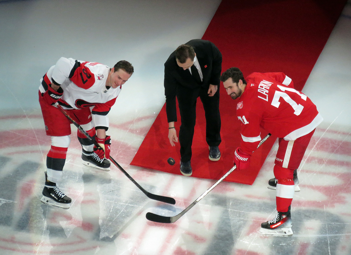 Andrei Svechnikov of the Carolina Hurricanes and Dylan Larkin of the Detroit Red Wings take a ceremonial faceoff from Sergei Fedorov as part of Fedorov's jersey retirement ceremony.