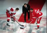 Andrei Svechnikov of the Carolina Hurricanes and Dylan Larkin of the Detroit Red Wings prepare for a ceremonial faceoff with Sergei Fedorov as part of Fedorov's jersey retirement ceremony.